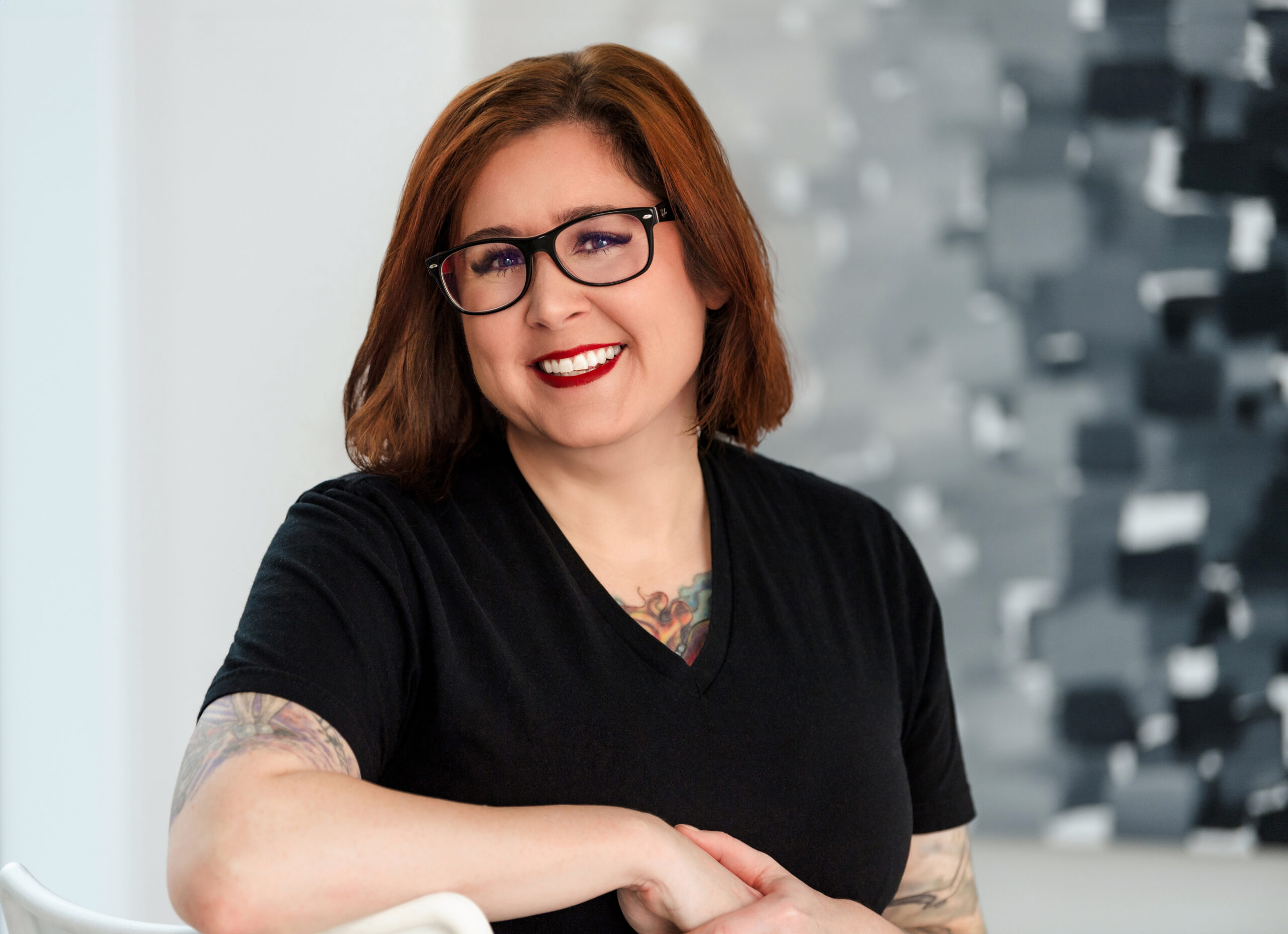 A picture of a woman with shoulder length brown hair, with a black shirt and black glasses.
